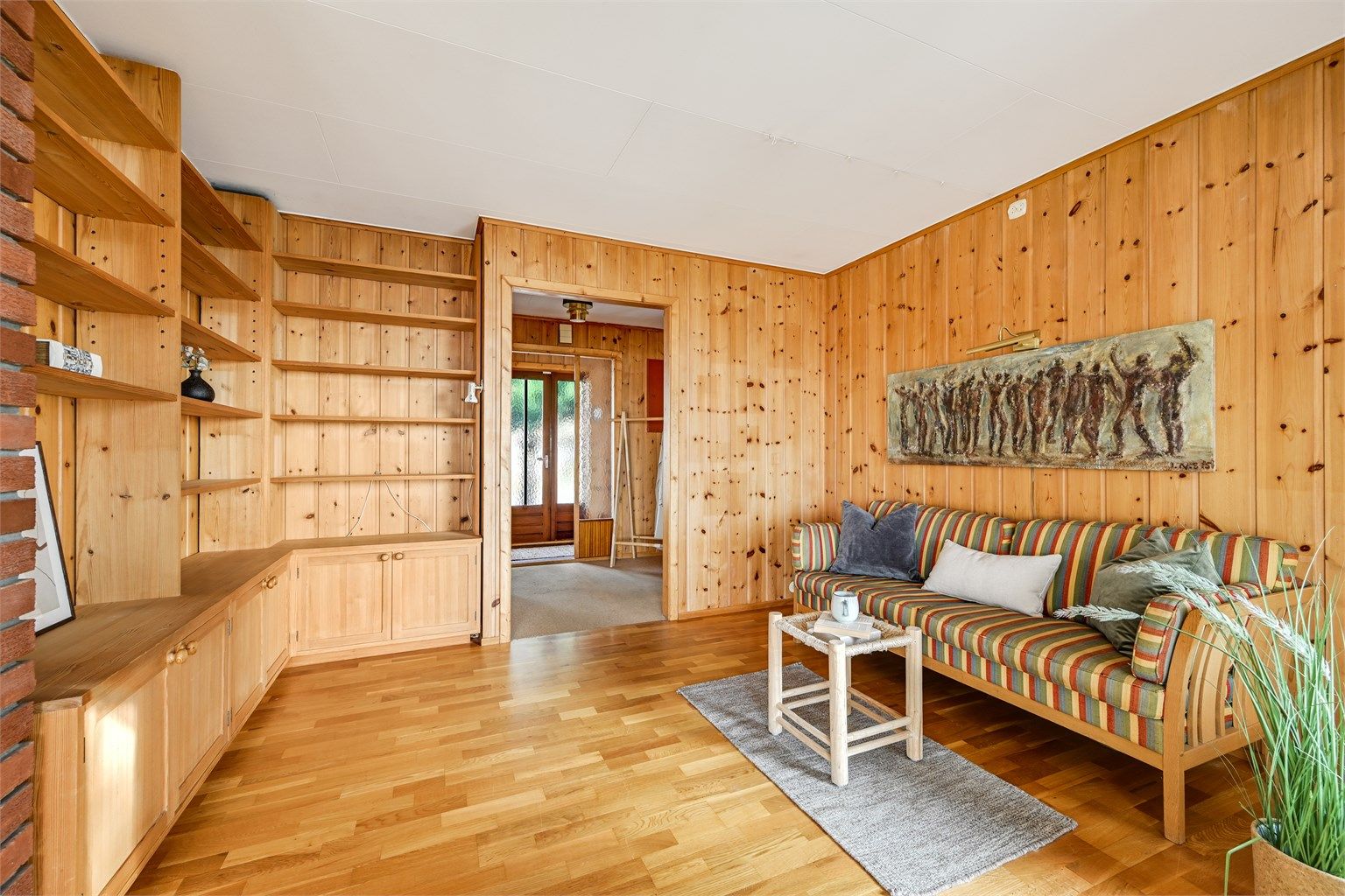Stue med lun og varm atmosfære, preget av flotte trepaneler og gode oppbevaringsløsninger i innebygde hyller.