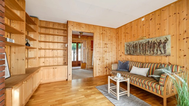 Stue med lun og varm atmosfære, preget av flotte trepaneler og gode oppbevaringsløsninger i innebygde hyller.