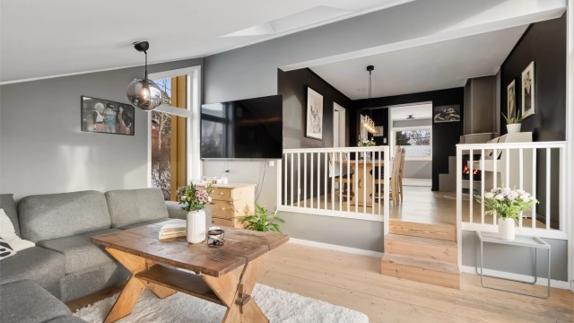 Stuen er et lyst og romslig oppholdsrom med tregulv og flere vinduer.