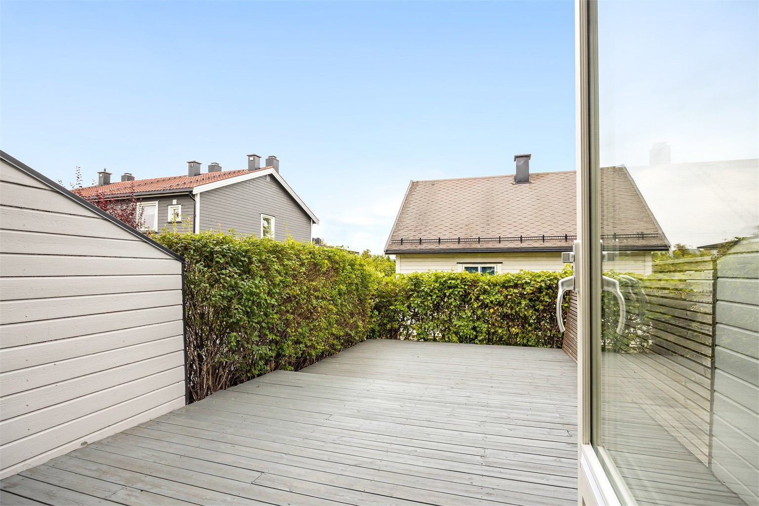 Terrassen er omkranset og skjermet med rekkverk, levegger og hekk.