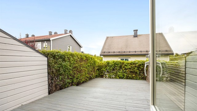 Terrassen er omkranset og skjermet med rekkverk, levegger og hekk.