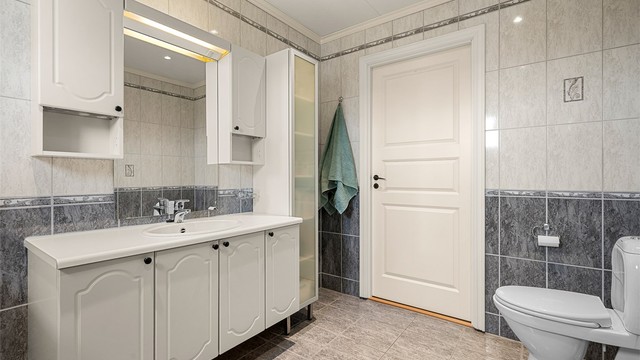 Badet har en praktisk planløsning med god skapplass, servantinnredning og toalett. De lyse overflatene gir rommet et ryddig uttrykk.