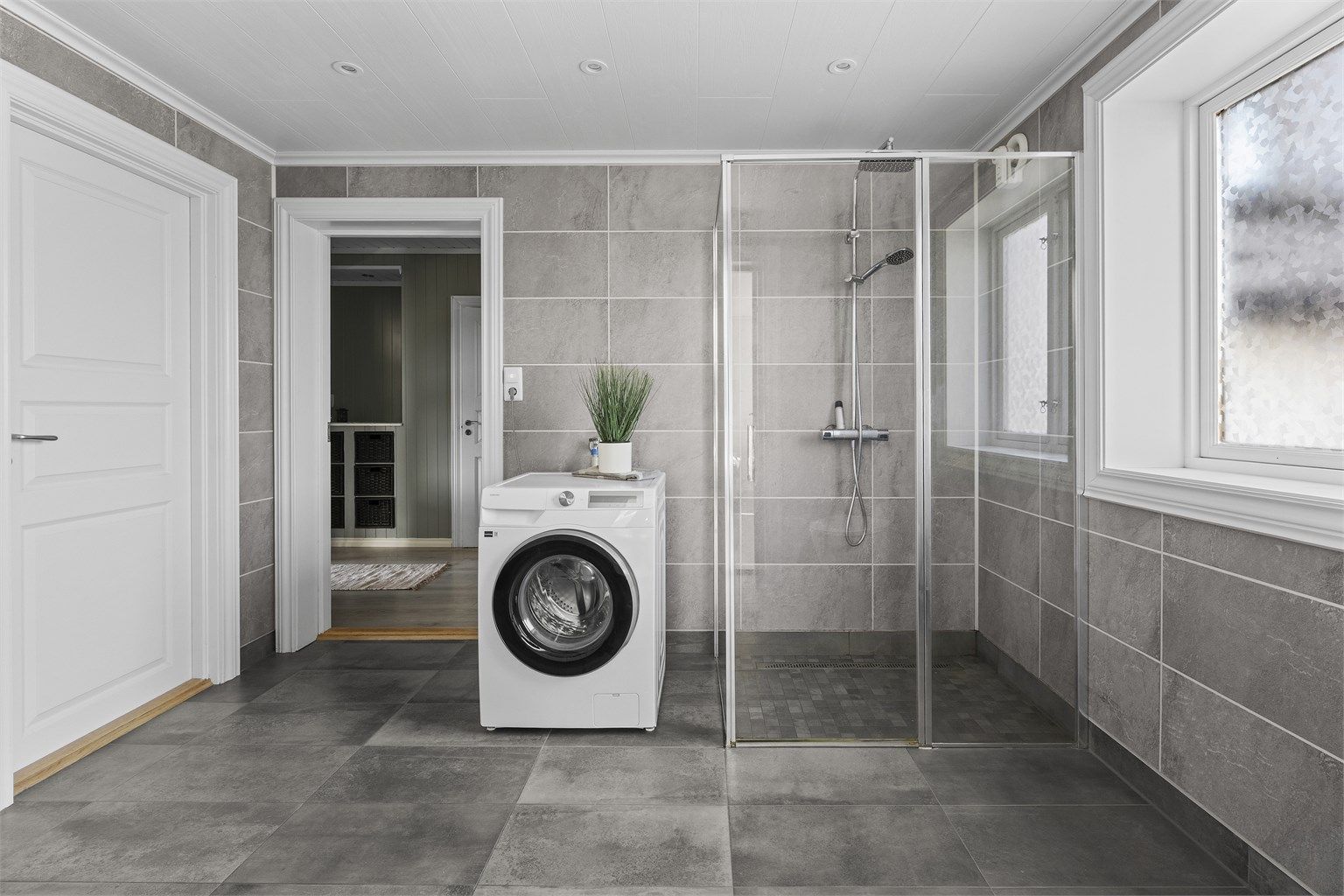 Badet er innredet med vegghengt servantskap med skuffer, speilskap med overlys, dusj på gulv og vegghengt toalett med innebygget sisterne.