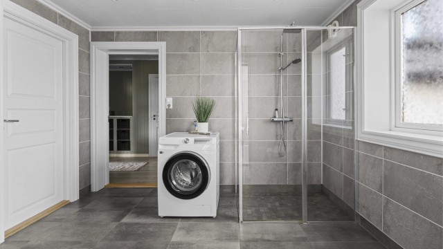 Badet er innredet med vegghengt servantskap med skuffer, speilskap med overlys, dusj på gulv og vegghengt toalett med innebygget sisterne.