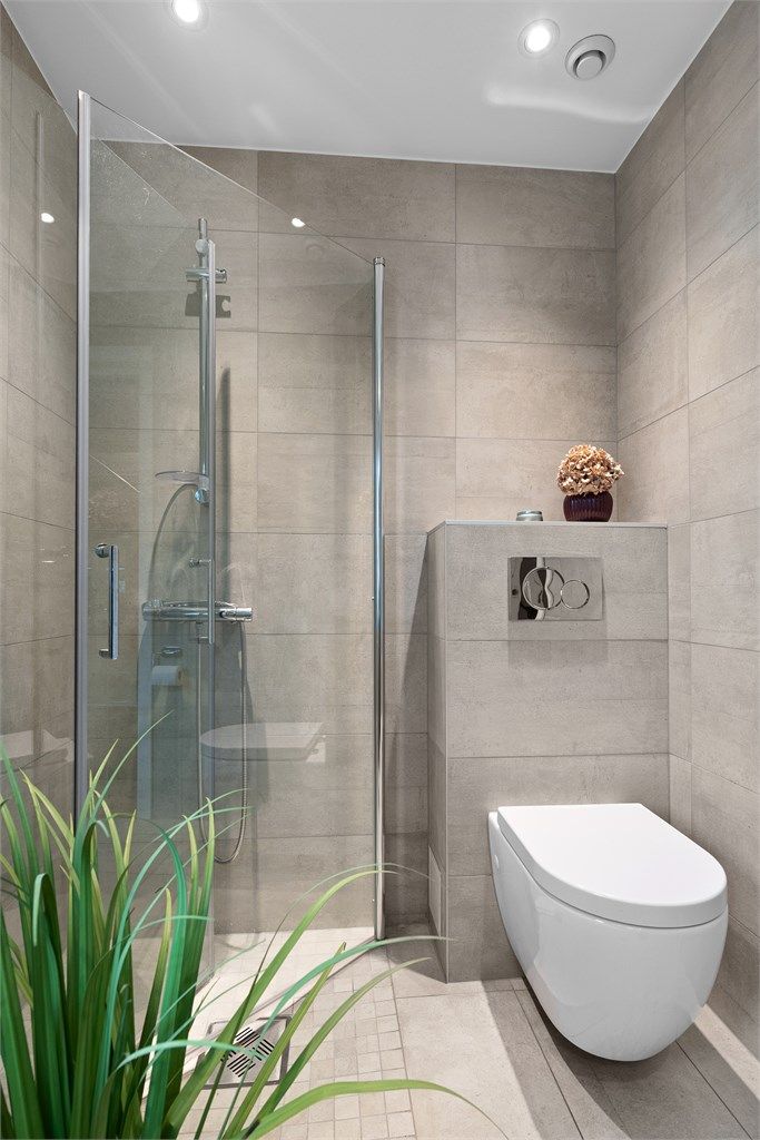 Badet har vegghengt toalett og dusjhjørne med glassdører.