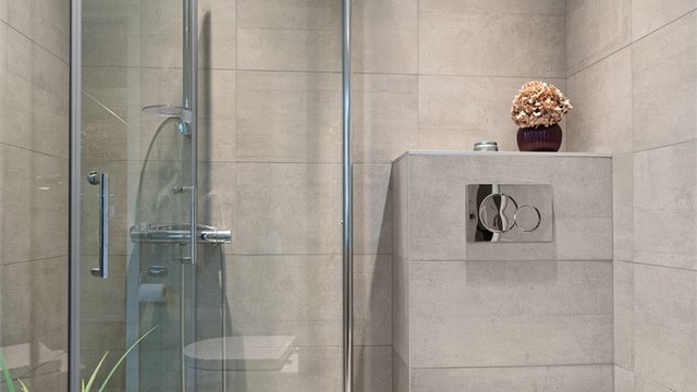Badet har vegghengt toalett og dusjhjørne med glassdører.