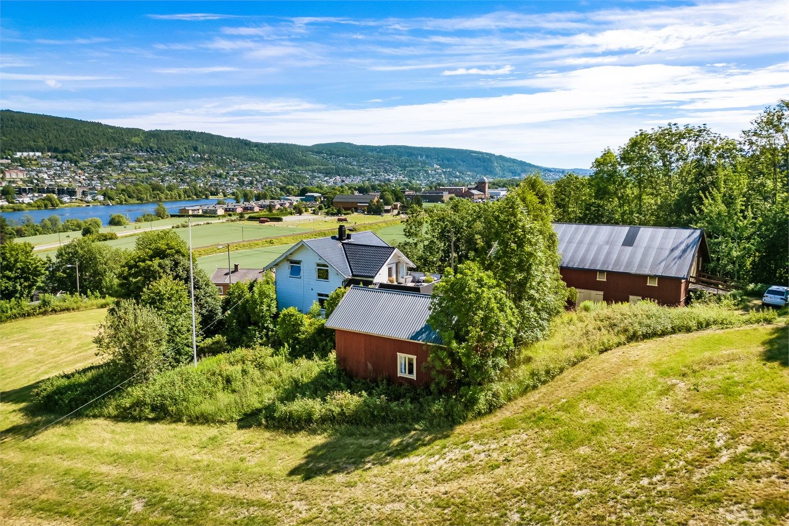 Småbruket ligger tilbaketrukket på en skrånende tomt med skog tett innpå i bakkant og åpne jordbruksarealer rundt. 
Foto: Knipzet AS - Emmy af Geijerstam