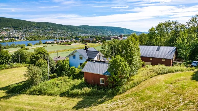 Småbruket ligger tilbaketrukket på en skrånende tomt med skog tett innpå i bakkant og åpne jordbruksarealer rundt.
Foto: Knipzet AS - Emmy af Geijerstam