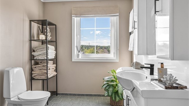 Badet har flislagt gulv med gulvvarme og en romslig servantinnredning med speil og overlys.