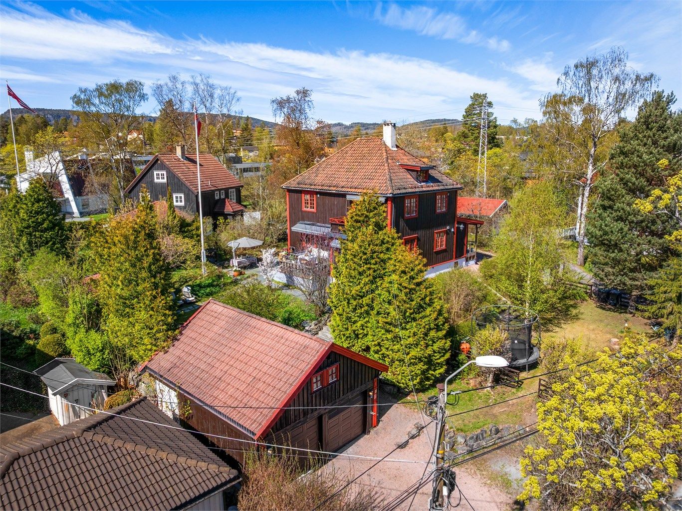 Oversikt over eiendommen med hovedhus, garasjer og den parkmessige hagen.