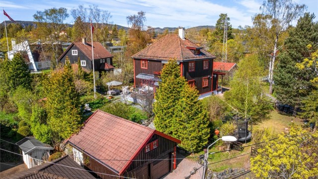 Oversikt over eiendommen med hovedhus, garasjer og den parkmessige hagen.
