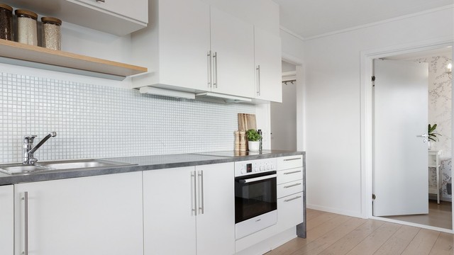 Kjøkkeninnredning har slette, lyse fronter, laminat benkeplate og mosaikkfliser over benken.