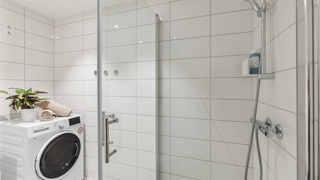 Badet er innredet med vegghengt klosett, servant med innredning, speil med lys og dusjhørne med svingbare dusjdører