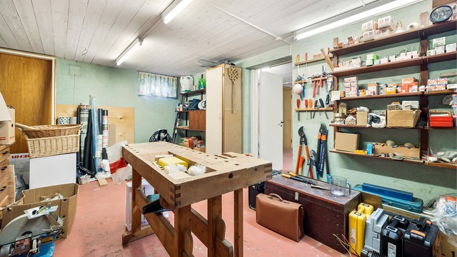 Verkstedrom i kjelleren med arbeidsbenk og rikelig med hylleplass.