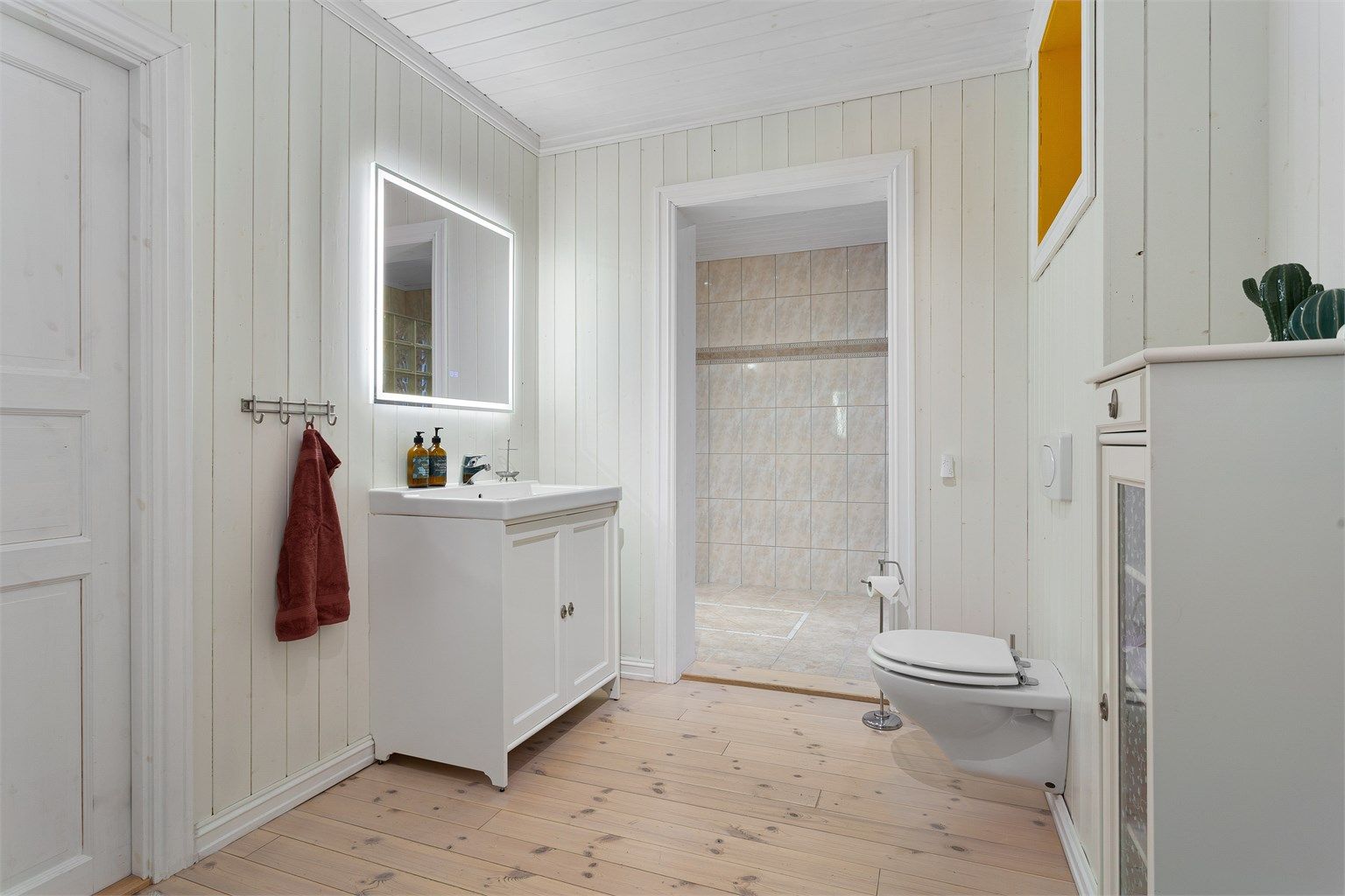 Romslig bad bestående av to deler. Innredet med gulvstående innredning med servant. Speil over servant med integrert lys. Vegghengt toalett.