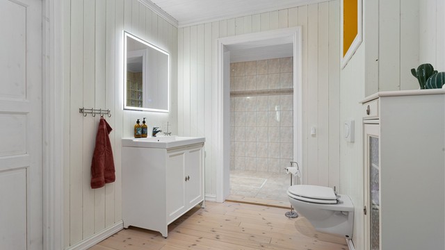 Romslig bad bestående av to deler. Innredet med gulvstående innredning med servant. Speil over servant med integrert lys. Vegghengt toalett.