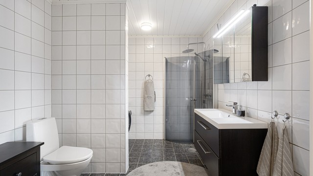 Romslig bad med flislagt gulv med varmekabler. Innredningen består av servantskap, speilskap og gulvmontert toalett.