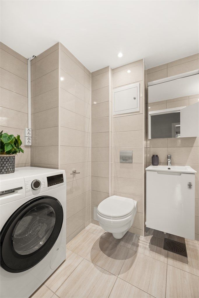 Badet er utstyrt med vegghengt toalett, speilskap og servant med underskap. Det er opplegg for vaskemaskin. Fordelerskap for rør-i-rør-systemet er også plassert her.