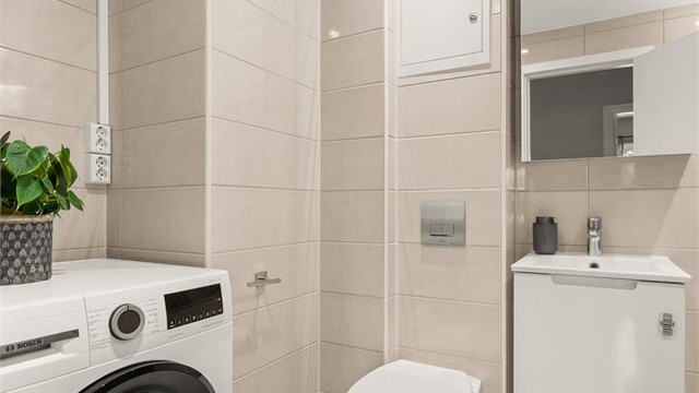 Badet er utstyrt med vegghengt toalett, speilskap og servant med underskap. Det er opplegg for vaskemaskin. Fordelerskap for rør-i-rør-systemet er også plassert her.