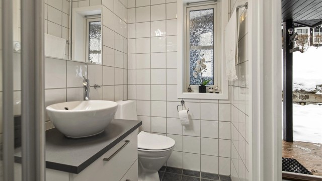 Badet er innredet med toalett, dusjhjørne og servant i innredning