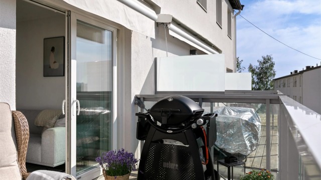 Balkongen har terrassebord og rekkverk i metall og glass.
