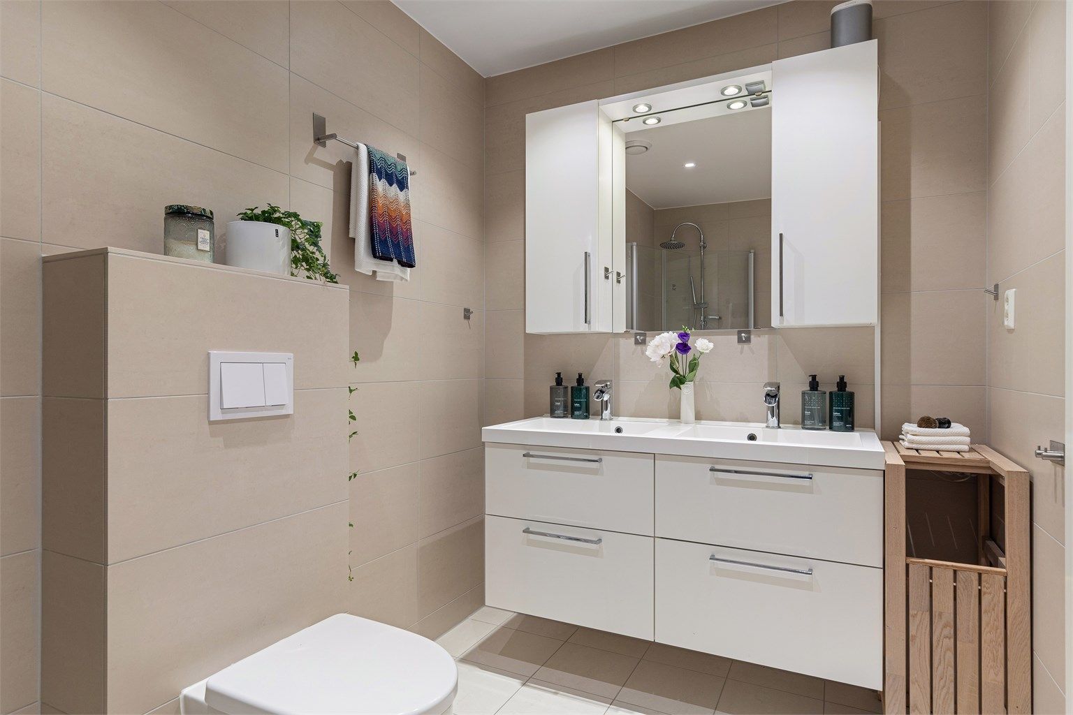 Badet er innredet med vegghengt toalett, dobbelt servant med underliggende skuffer, samt dusjhjørne med innfellbare dusjvegger i glass.