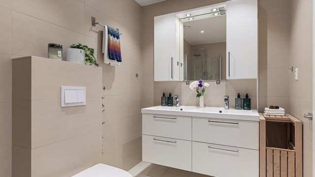 Badet er innredet med vegghengt toalett, dobbelt servant med underliggende skuffer, samt dusjhjørne med innfellbare dusjvegger i glass.