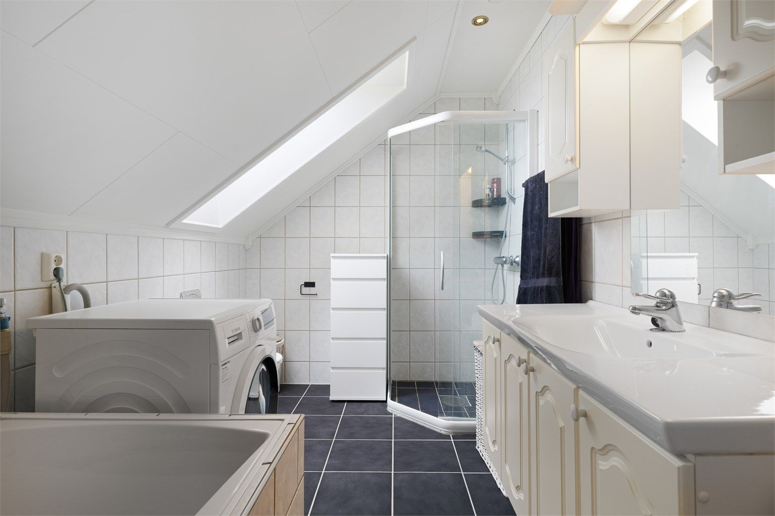 Pent flislagt bad på 6 kvm med gulvvarme, downlights og opplegg for vaskemaskin. Videre er badet utstyrt med servantskap med overskap og speil med lys, vegghengt toalett, dusjhjørne og badekar.