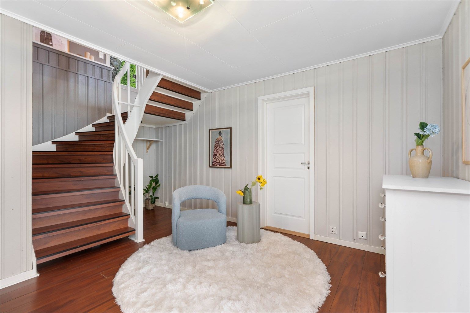 Romslig hall i underetasjen med trapp opp til hovedetasjen.