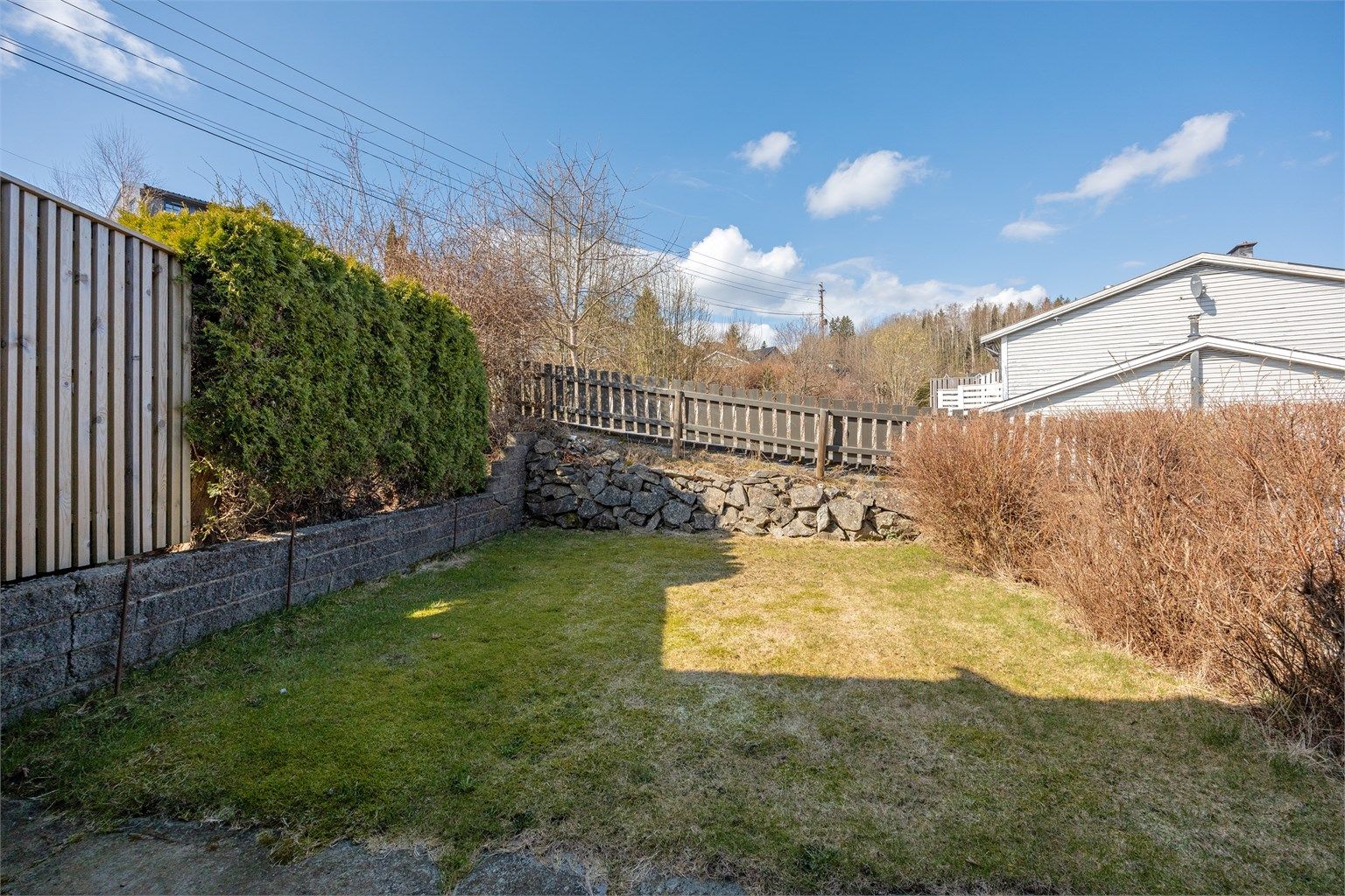 Tomten er opparbeidet med gressplen, hekk og en forstøtningsmur av lettklinkerblokker mot nabo.