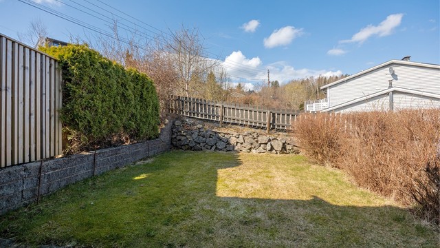 Tomten er opparbeidet med gressplen, hekk og en forstøtningsmur av lettklinkerblokker mot nabo.