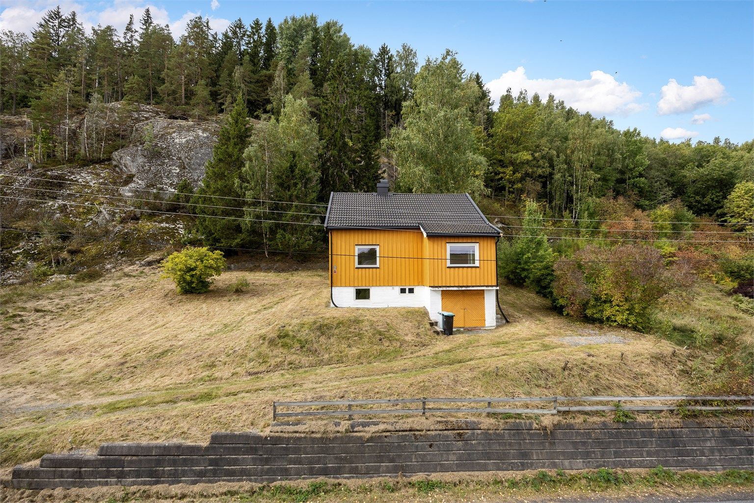 Forstøtningsmur av betongstein avgrenser eiendommen mot veien.