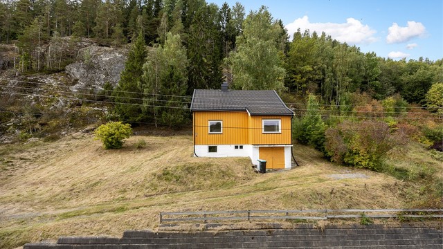 Forstøtningsmur av betongstein avgrenser eiendommen mot veien.