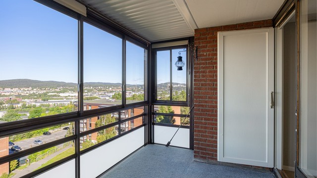 Innglasset balkong med teppebelagt gulv og plass til sittegruppe.