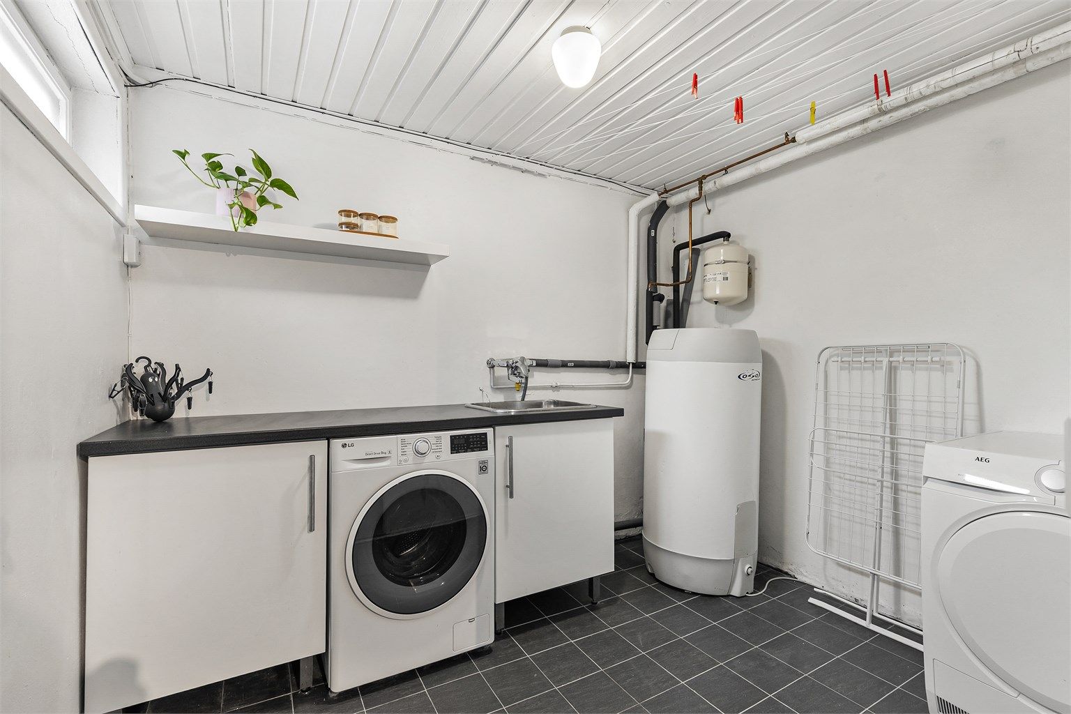 Vaskerom med flislagt gulv og malte veggflater. Gulvstående benkeskap. Benkeplate av laminat. Nedfelt utslagsvask og vegghengt armatur. Opplegg for vaskemaskin under benkeplate. Varmtvannsbereder plassert i hjørne. Naturlig avtrekksventil.
