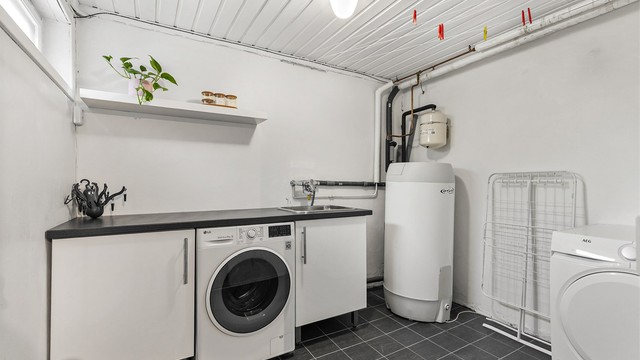 Vaskerom med flislagt gulv og malte veggflater. Gulvstående benkeskap. Benkeplate av laminat. Nedfelt utslagsvask og vegghengt armatur. Opplegg for vaskemaskin under benkeplate. Varmtvannsbereder plassert i hjørne. Naturlig avtrekksventil.
