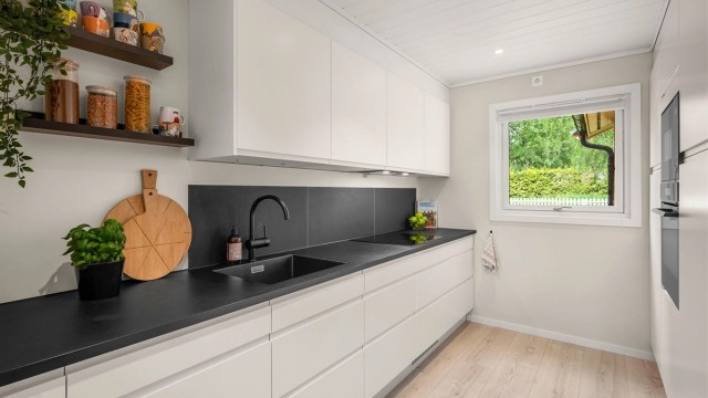 Kjøkkenet ligger naturlig tilbaketrukket fra stuen og er innredet med lyse slette flater og benkeplate i kontrast.