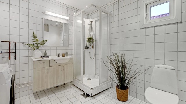 Bad - flislagt gulv og vegger, malt himling - gulvvarme - downlights i himling - baderomsinnredning (servant med underskap og speil) - dusjkabinett - toalett - opplegg til vaskemaskin
