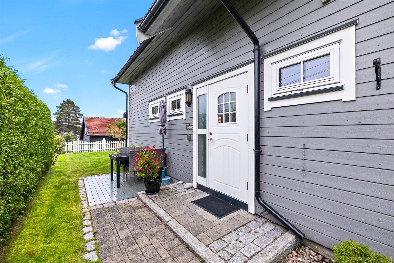 Inngangspartiet er pent opparbeidet med belegningsstein og trapp. Det er god plass til krukker og blomster som setter en hyggelig ramme rundt inngangen. Like ved finner du en liten, skjermet platting – perfekt for en sittegruppe eller en rolig kaffepause.