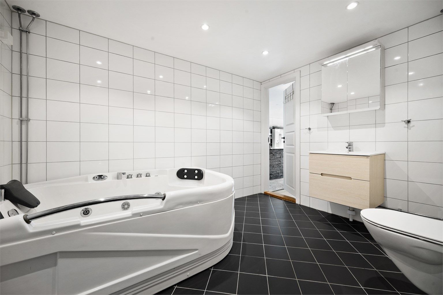 Badet er innredet med vegghengt servantinnredning med speilskap over servant. Videre er det vegghengt toalett, hjørneboblebadekar og dusjhjørne.