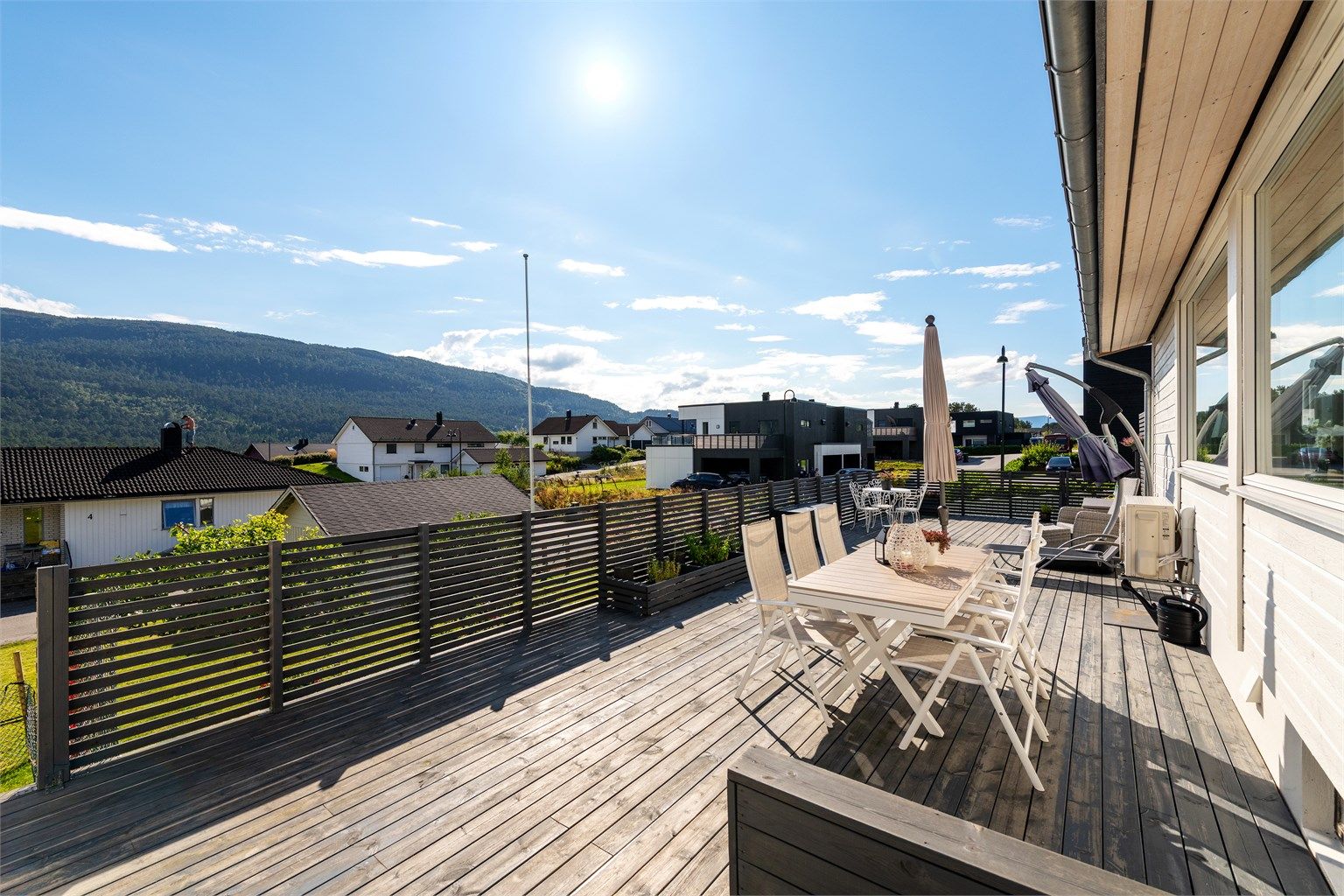 Stor tilbygget terrasse mot sydvest med flere soner og sittegrupper. Det er trapp fra terrassen til hage og plen mot syd