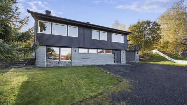 Fasaden mot adkomsten har stående trekledning og integrert garasje i underetasjen.