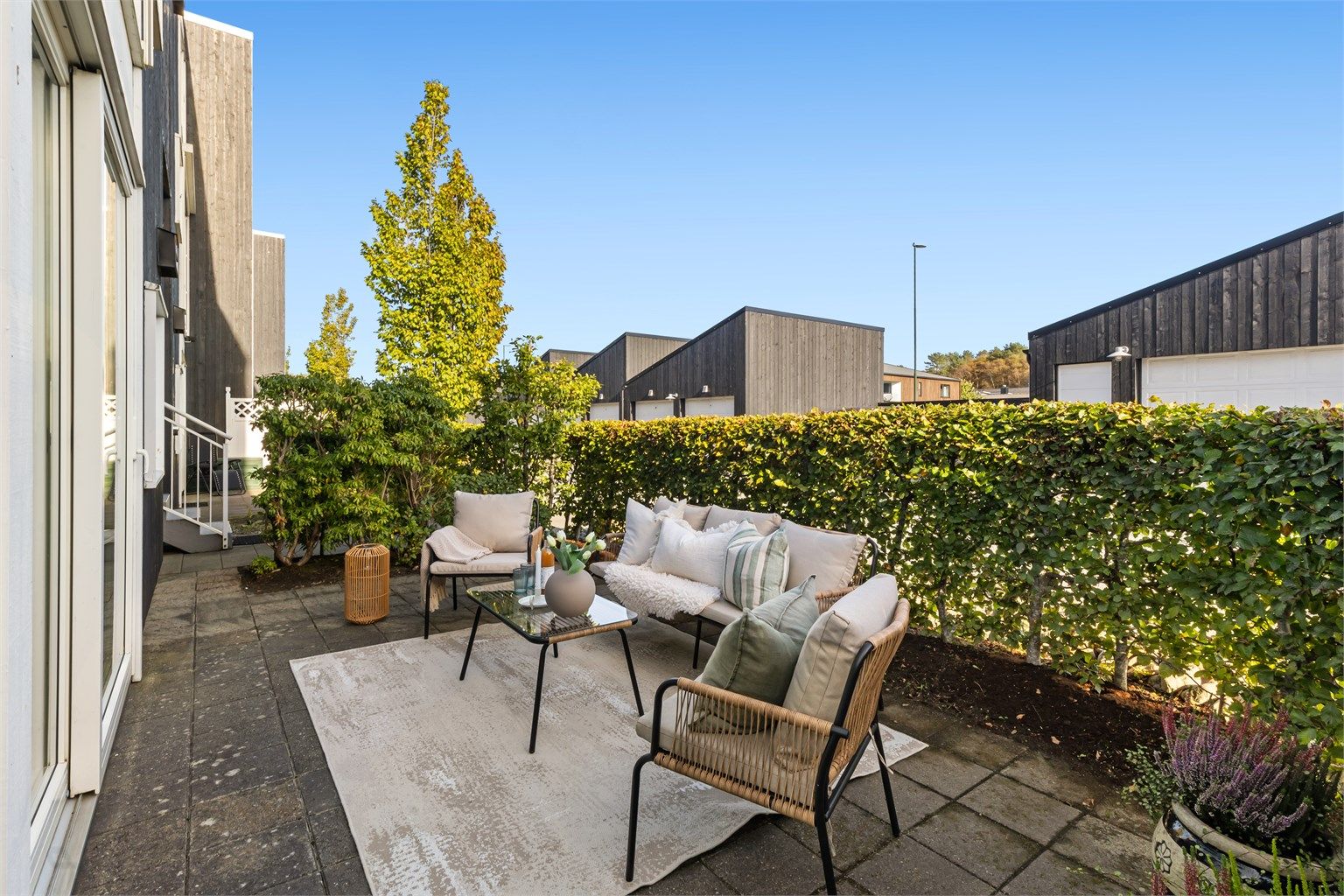 Hellelagt markterrasse skjermet av hekk, med god plass til utendørs sittegruppe.