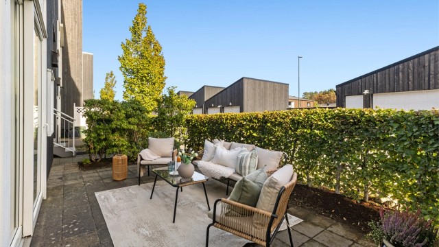 Hellelagt markterrasse skjermet av hekk, med god plass til utendørs sittegruppe.
