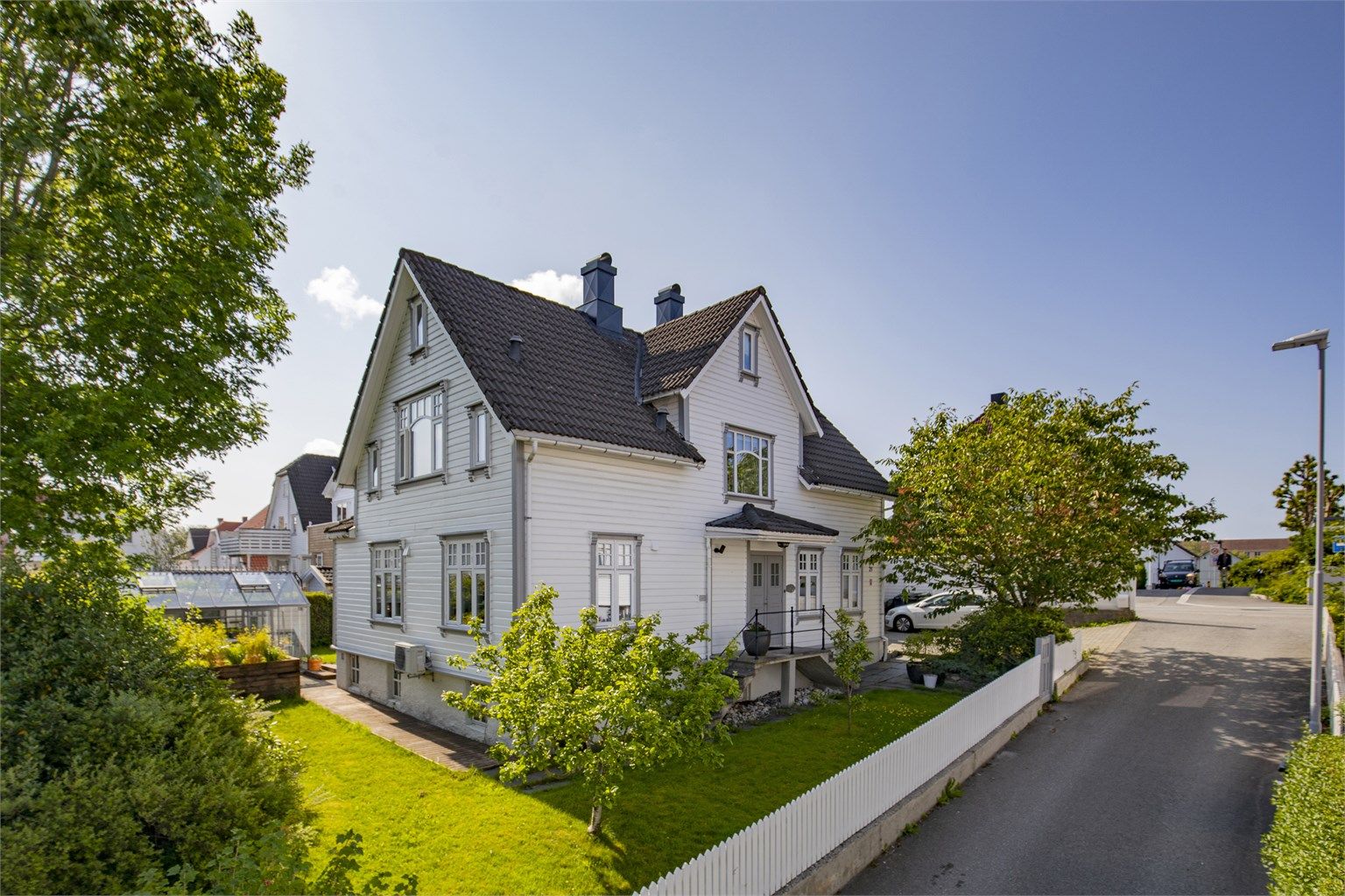 Eiendommen sett fra gaten, med en velholdt hage og hvitt stakittgjerde.