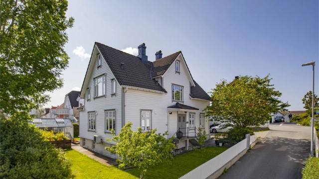 Eiendommen sett fra gaten, med en velholdt hage og hvitt stakittgjerde.