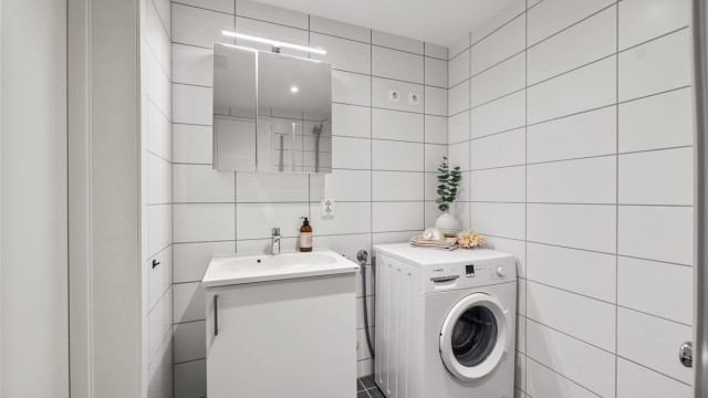 Badet er utstyrt med vegghengt toalett, dusjhjørne og servant med speilskap.