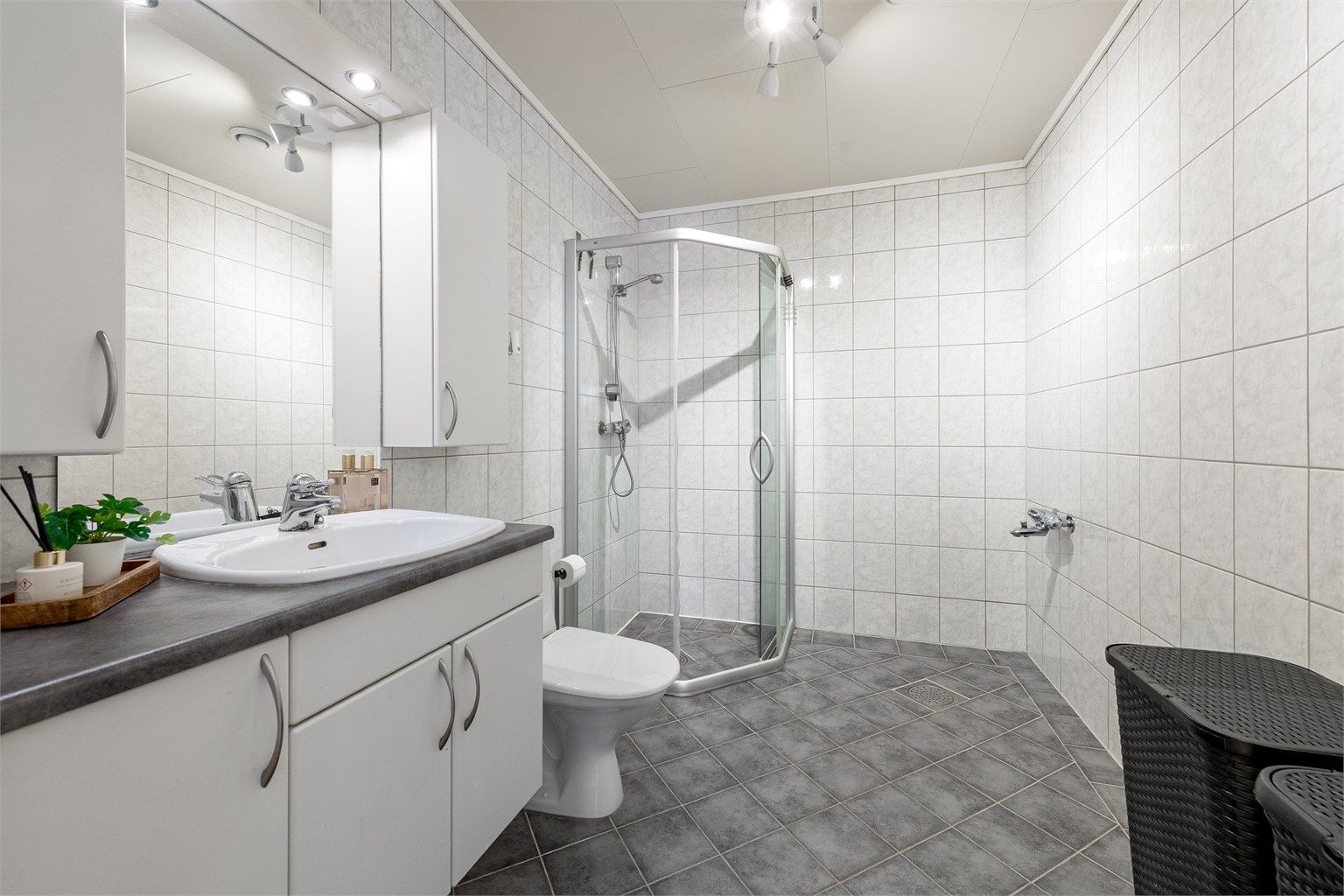 Badet har flislagt gulv med gulvvarme, flislagte vegger og et dusjhjørne med skyvedører. Rommet er klargjort for badekar.