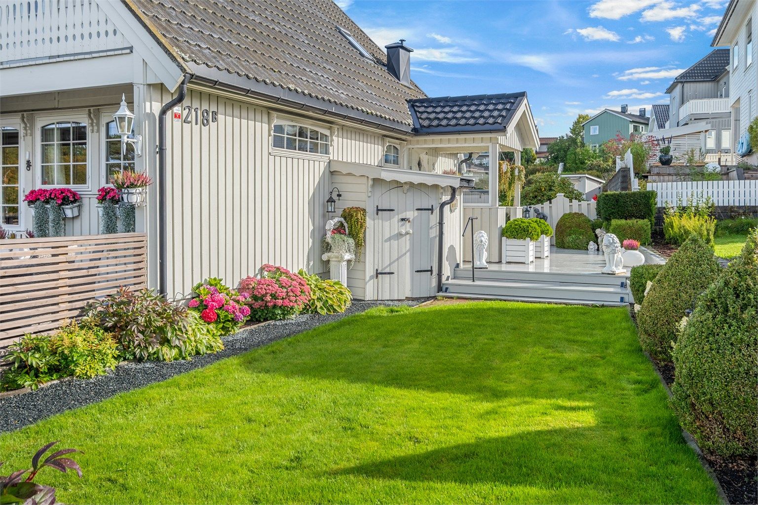 Skjermet hage med grønne plenarealer og beplantede bed langs husveggen.