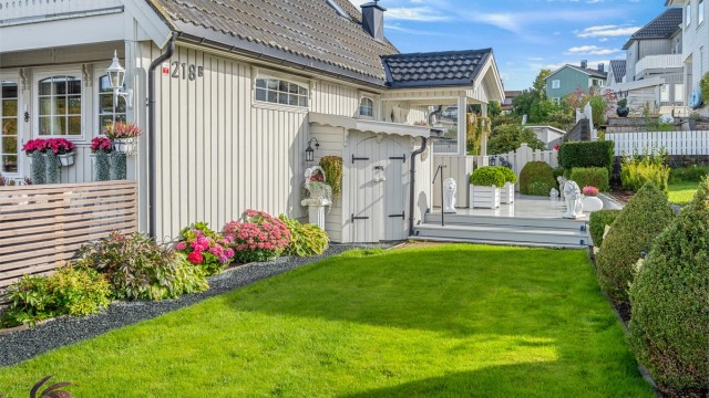 Skjermet hage med grønne plenarealer og beplantede bed langs husveggen.